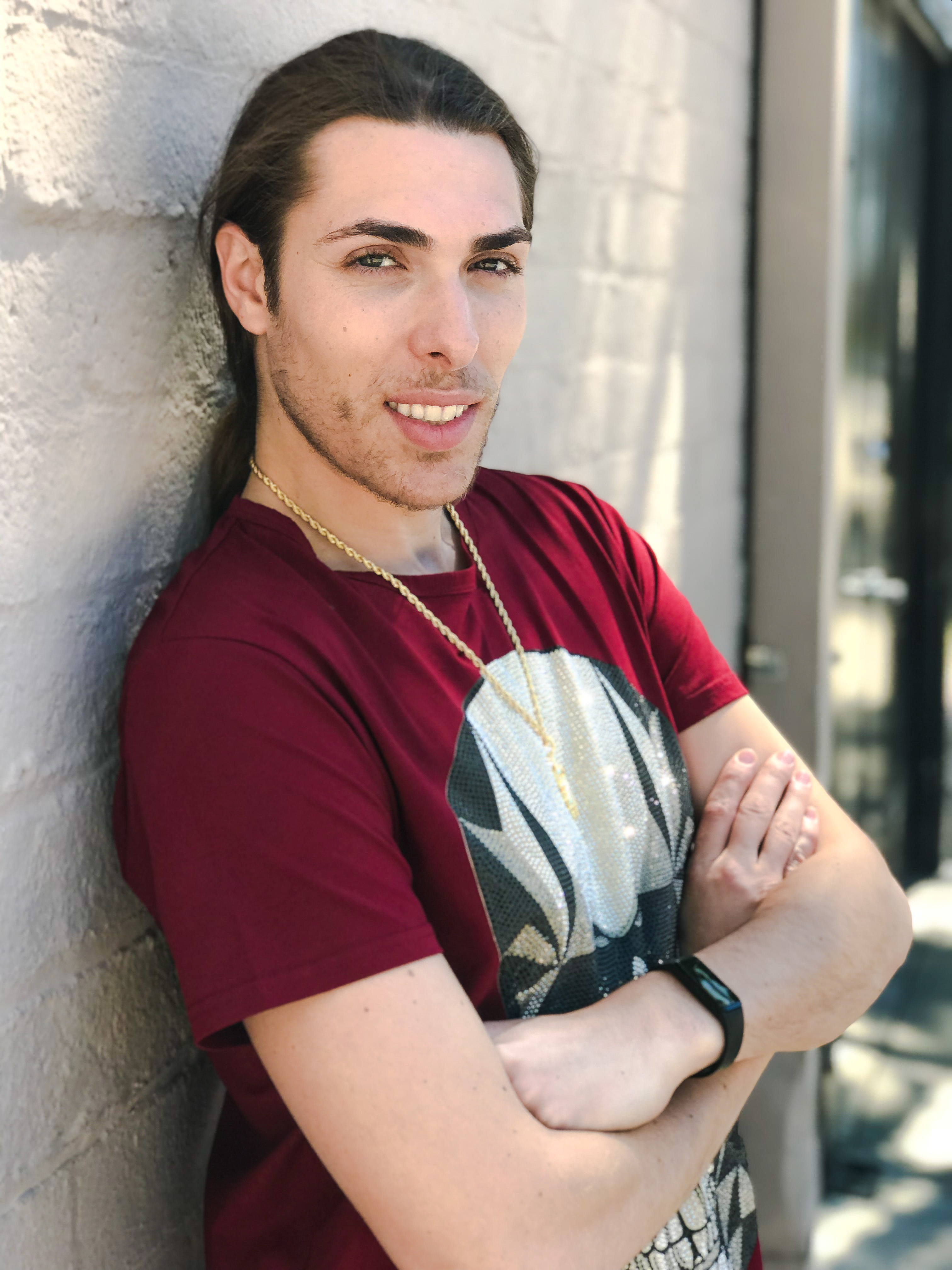 Alex Veach (Alexander Veach) LA streetwear, burgundy graphic tee, warm smile on white wall.