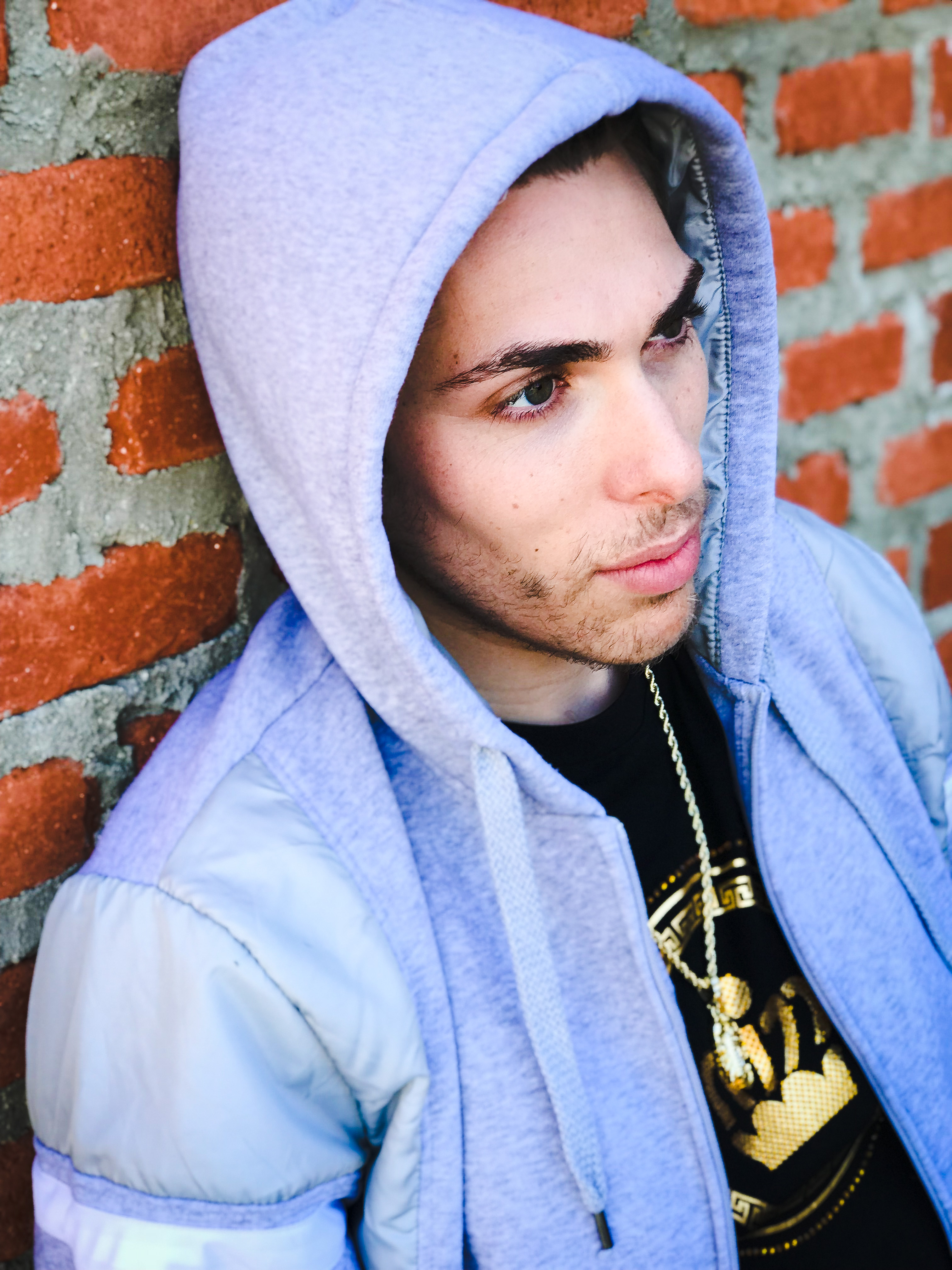 Alex Veach (Alexander Veach) LA streetwear, grey hoodie up with gold chain, brick wall.