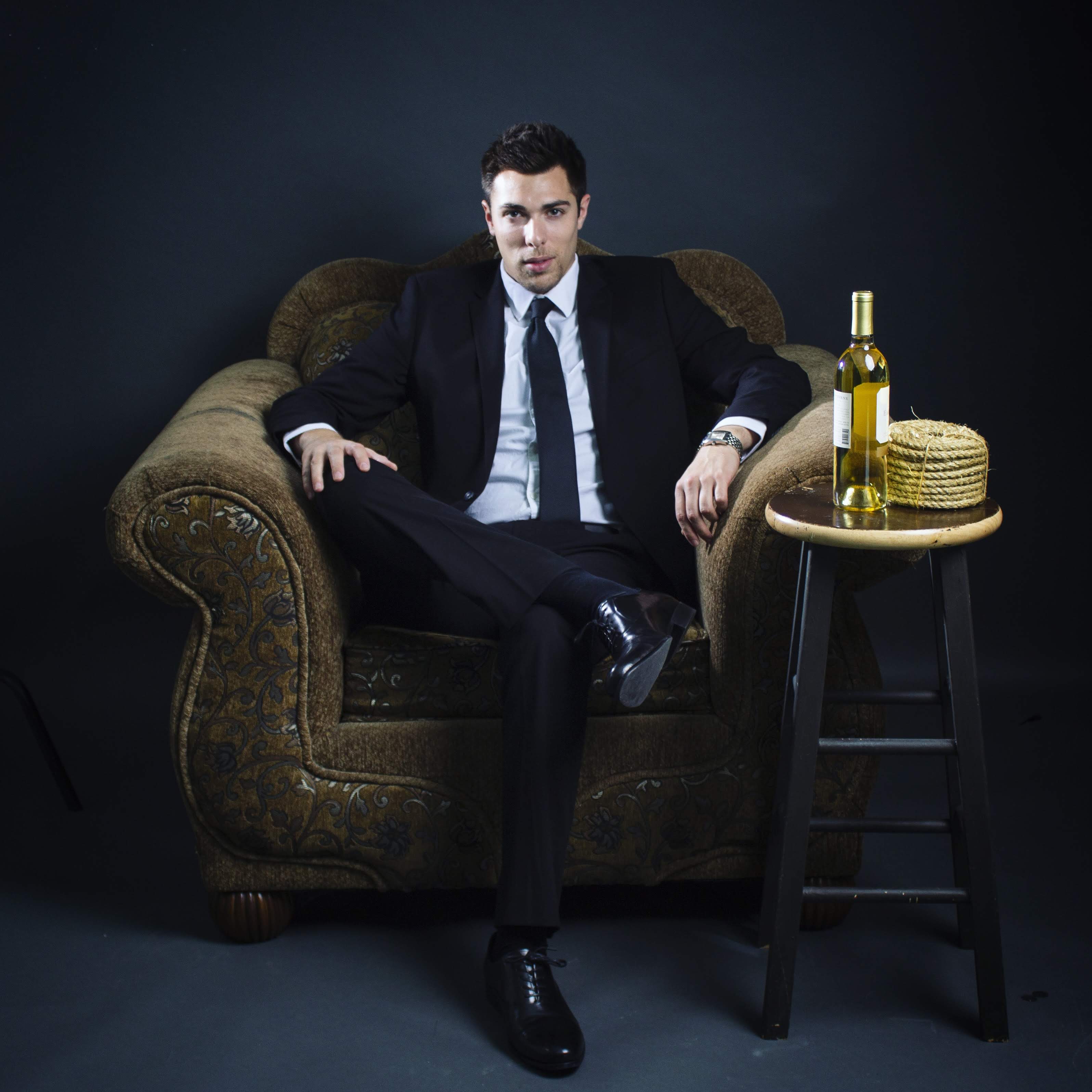 Alex Veach (Alexander Veach) cinematic black-suit editorial, seated on ornate armchair in moody studio.